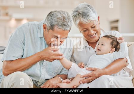 Liebe, Großeltern und Baby auf Sofa zu Hause mit Küssen, Spielen und Binden mit einem Lächeln im Wohnzimmer. Glückliche Familie, Senioren und Enkelkinder Stockfoto