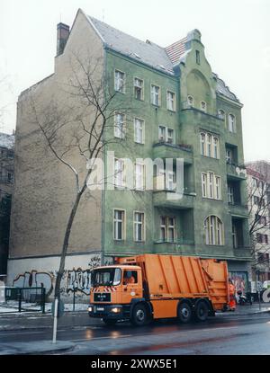Auf einer Straße vor einem alten, grünen Wohngebäude mit Graffiti an den Mauern in Berlin steht ein knalloranger Müllwagen. Dieses Bild aus dem Jahr 2005 zeigt die Bemühungen um die Sauberkeit in der Stadt. Stockfoto
