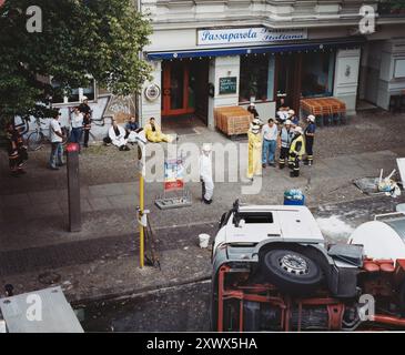 Ein Bild von Notfallhelfern in Schutzausrüstung, die einen umgekippten Lkw auf einer Straße in Berlin 2005 betreuen. Die Leute beobachten und warten in der Nähe vor einem Restaurant. Stockfoto