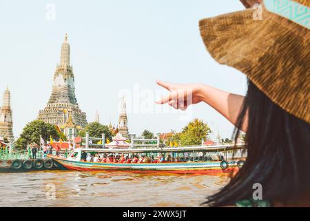 Bangkok, Thailand - 11. februar 2024: kaukasierin zeigt mit dem Finger auf den buddhistischen Tempel Wat Wrun. Boote legen am Pier vor dem berühmten Wahrzeichen von Siam an Stockfoto