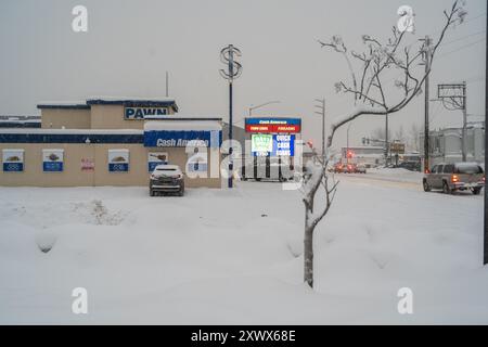 Das Bild zeigt eine schneebedeckte Pfandwerkstatt mit einem hell erleuchteten Barkreditschild in Anchorage, Alaska, während des Winters. Die Szene ist kalt und desolat und steht für finanzielle Schwierigkeiten und Kampf. Stockfoto
