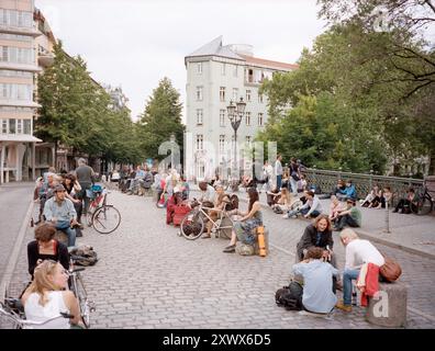 Eine lebhafte Szene auf der Admiralbrücke in Berlin-Kreuzberg, 2011, in der eine lebhafte Menschenmenge an einem Freitagabend zu sehen ist. Das Bild fängt das Wesen von Gemeinschaft, Freizeit und urbanem Leben ein, während sich einzelne entspannen, Kontakte knüpfen und die Sommeratmosphäre genießen. Stockfoto