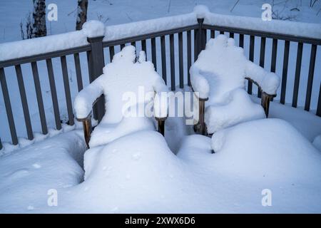 Eine ruhige Winterszene mit schneebedeckten Terrassenstühlen, die metaphorisch an sitzende Menschen erinnern. Der Schnee bedeckt die Stühle und schafft eine friedliche, isolierte Atmosphäre, die typisch für einen Alaska Winter ist. Stockfoto