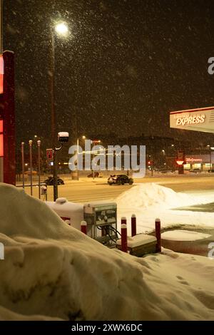 Eine verschneite Nachtszene an einer Tankstelle in Anchorage, Alaska. Das Bild fängt die ruhige, aber kalte Atmosphäre einer Winternacht mit frischem Schneefall ein und sorgt für eine ruhige und ruhige Stimmung. Stockfoto