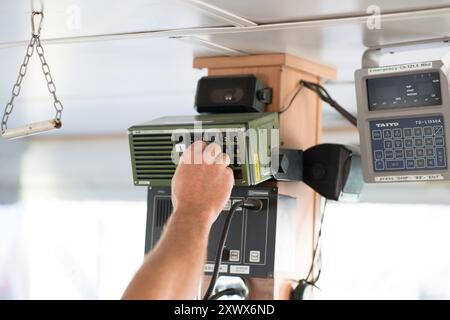 Eine Nahaufnahme einer Hand, die ein Funkbedienfeld in einem Schiff bedient. Das Bild zeigt die maritime Technologie, die in den Bereichen Navigation und Sicherheit eingesetzt wird. Unverzichtbar für die Kommunikation auf See und das Notfallmanagement. Stockfoto