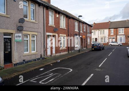 Eine ruhige Straße mit Reihenhäusern und geparkten Autos in Wallsend, Newcastle upon Tyne. Das Bild zeigt ein typisches Wohngebiet, das Gemeinschafts- und Alltagsleben hervorhebt. Ein Schild „verkauft“ ist sichtbar, das auf die letzten Änderungen an der Immobilie hinweist. Stockfoto