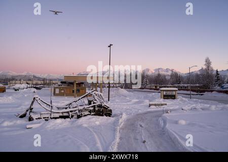 Malerischer Winterblick in der Nähe des Merrill Field Airport, Anchorage, Alaska, mit schneebedecktem Boden, fernen Bergen, und ein Flugzeug, das am Himmel fliegt. Dieses Bild weckt Gefühle von Reisen, Ruhe und friedlicher Natur. Stockfoto