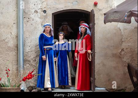 Jaunpils, Lettland – 10. August 2024: Frauen in Kostümen versammeln sich vor der Tür eines alten Gebäudes. Stockfoto