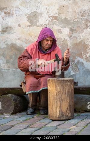 Jaunpils, Lettland – 10. August 2024: Ein geschickter Handwerker formt Metall mit einem Hammer an einem Holzstumpf. Stockfoto