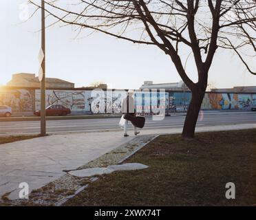 Ein einsamer Mann, der 2005 die East Side Gallery in Berlin durchläuft. Er kommt an einem sonnigen Tag an farbenfrohen Graffiti vorbei. Die Szene fängt die urbane Kunstkultur und ihre historische Essenz ein. Stockfoto