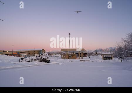 Majestätische Winterszene mit einem kleinen Flugzeug, das über eine schneebedeckte Stadt in der Nähe des Merrill Field Airport in Anchorage, Alaska, fliegt. Dieses Bild fängt die Ruhe der schneebedeckten Landschaft mit einem ruhig geparkten Lkw ein. Stockfoto