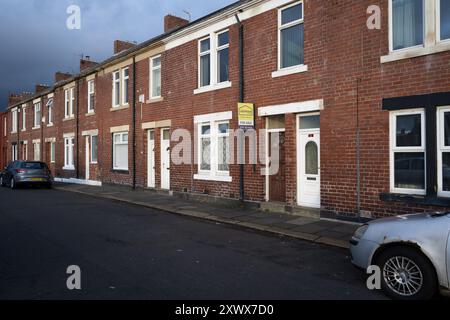 Reihenhäuser in einer ruhigen Wohnstraße in Wallsend, Newcastle upon Tyne. Ein Haus hat ein Schild zum Verkauf, das neue Chancen und Veränderungen darstellt. Perfekt für Themen wie städtisches Wohnen, Immobilien und Wohneigentum. Stockfoto