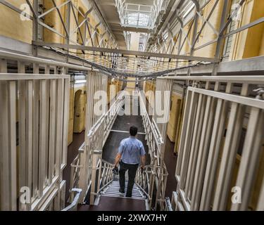 Ein Gefängniswärter geht durch die historischen und imposanten Gänge des Tegel Gefängnisses in Berlin-Reinickendorf. Dieses Bild fängt einen Moment in Deutschlands größter geschlossener Justizvollzugsanstalt ein, der Einsamkeit und Disziplin symbolisiert. Stockfoto