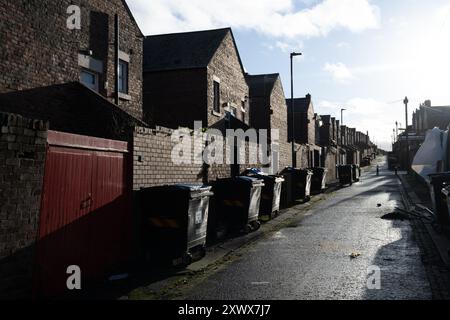 Eine friedliche, leere Gasse in Fenham, Newcastle upon Tyne. Backsteinhäuser säumen beide Seiten der Straße mit Mülltonnen, die ordentlich im Freien angeordnet sind. Das Bild weckt Gefühle der Einsamkeit und den Alltag des urbanen Lebens. Stockfoto