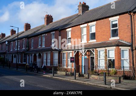 Eine malerische Reihe traditioneller Reihenhäuser in Fenham, Newcastle upon Tyne. Die warmen Ziegelfassaden und die Anwesenheit von Fußgängern schaffen eine charmante und einladende Straßenszene. Stockfoto