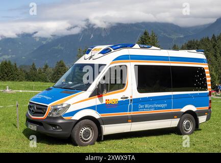 Oberstdorf, Deutschland. August 2024. Vor den bewölkten Bergen steht auf der Alpe Dornach ein Rettungswagen der ASB (Arbeitersamaritanischer Bund). Unter dem Motto „Dare to make Last wishes“ transportiert das ASB Patienten, die sich einer Behandlung unterziehen, an besondere Orte, um ihre letzten Wünsche zu erfüllen und besondere Erlebnisse zu ermöglichen. Quelle: Stefan Puchner/dpa/Alamy Live News Stockfoto