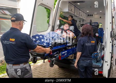 Oberstdorf, Deutschland. August 2024. Norbert Rzadki (l-r), Rima Schucht und Anita Sräga vom Arbeiter-Samariter-Bund (ASB) entladen Kerstin Lindemann, die auf einer Bahre liegt, aus einem Krankenwagen. Unter dem Motto „Dare to make Last wishes“ transportiert ASB Patienten, die sich einer Behandlung unterziehen, an besondere Orte, um ihre letzten Wünsche zu erfüllen und besondere Erlebnisse zu ermöglichen. Quelle: Stefan Puchner/dpa/Alamy Live News Stockfoto