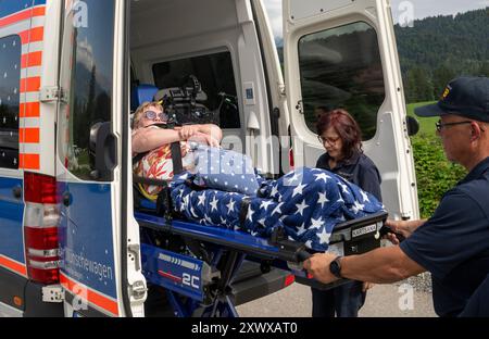 Oberstdorf, Deutschland. August 2024. Anita Sräga (Mitte) und Norbert Rzadki (rechts) vom Arbeiter-Samariter-Bund (ASB) laden Kerstin Lindemann, die auf einer Liege liegt, in einen Krankenwagen auf der Alpe Dornach. Unter dem Motto „Dare to make Last wishes“ transportiert die ASB Patienten, die sich einer Behandlung unterziehen, an besondere Orte, um ihre letzten Wünsche zu erfüllen und besondere Erlebnisse zu ermöglichen. Quelle: Stefan Puchner/dpa/Alamy Live News Stockfoto