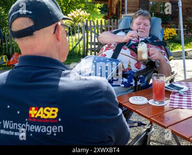 Oberstdorf, Deutschland. August 2024. Norbert Rzadki (l) vom Arbeiter-Sarmariter-Bund (ASB) ist bei Kerstin Lindemann, die auf einer Liege liegt, auf Alpe Dornach. Unter dem Motto „Dare to make Last wishes“ transportiert ASB Patienten, die sich einer Behandlung unterziehen, an besondere Orte, um ihre letzten Wünsche zu erfüllen und besondere Erlebnisse zu ermöglichen. Quelle: Stefan Puchner/dpa/Alamy Live News Stockfoto