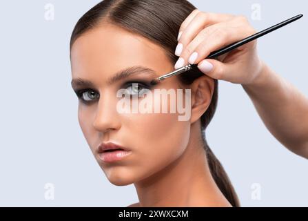 Porträt einer charmanten brünetten Frau mit gesunder, sauberer Haut, langen Haaren und rauchigen Augen Make-up. Make-up-Künstler wendet Lidschatten an. Der Begriff der Aesth Stockfoto