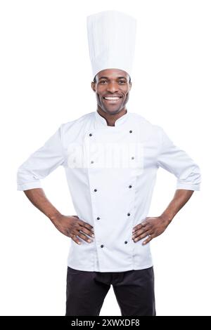 Kochen ist mein Leben! Selbstbewusster junger afrikanischer Koch in weißer Uniform, der Hände auf Hüften hält und lächelt, während er vor weißem Hintergrund steht Stockfoto