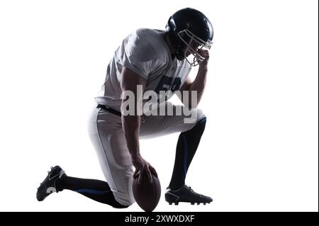 Vorbereitung auf großes Spiel. Seitenansicht eines American Football-Spielers, der die Hand auf dem Helm hält, während er auf dem Knie steht, vor weißem Hintergrund Stockfoto