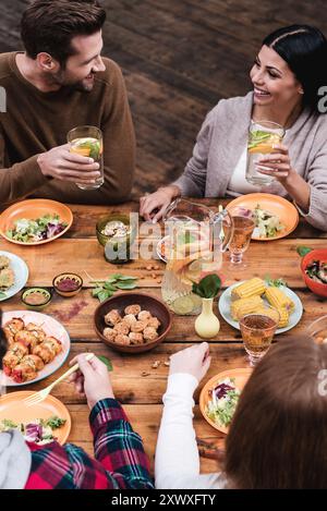 Essen mit Freunden. Blick von oben auf vier Personen, die zusammen zu Abend essen, während sie am rustikalen Holztisch sitzen Stockfoto
