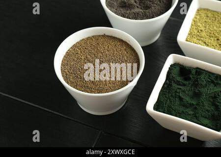 Verschiedene Superfood-Pulver in Schüsseln auf schwarzem Holztisch, Nahaufnahme Stockfoto