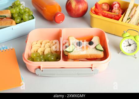 Lunchboxen mit Snacks, einer Flasche Saft, Wecker und Schreibwaren auf weißem Tisch Stockfoto