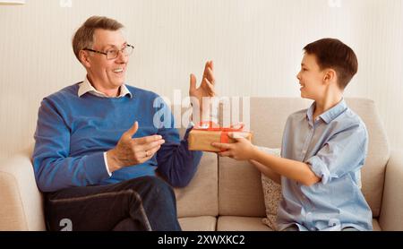 Junge Glückwunsch Opa Geben Geschenk Sitzen auf der Couch Indoor Stockfoto