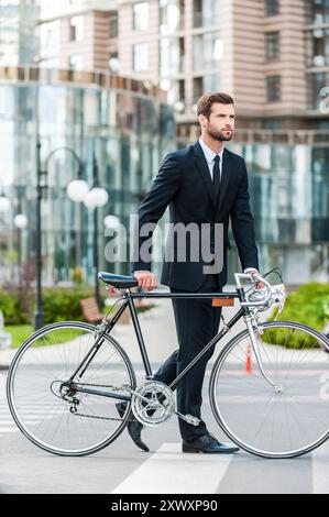 Geschäftsmann mit Fahrrad. Voller Länge eines hübschen jungen Geschäftsmannes, der sein Fahrrad rollte, während er die Straße überquerte Stockfoto