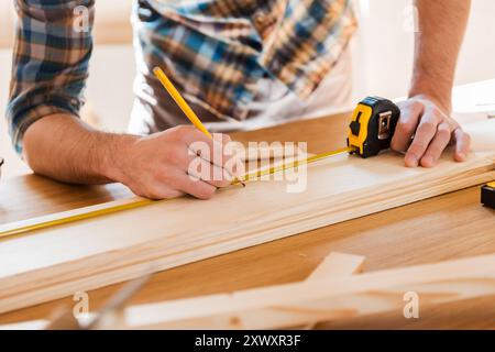 Exakte Messung. Nahaufnahme eines jungen Zimmermanns, der an der Holzdiele vermisst Stockfoto