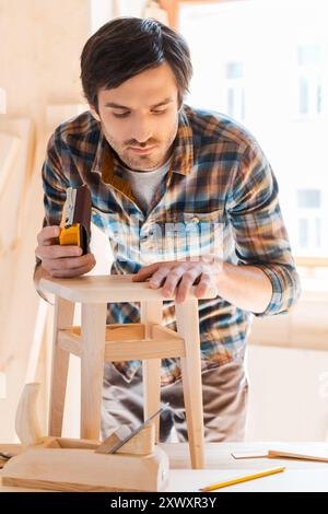 Mit Holz zu arbeiten, ist seine Leidenschaft. Konzentrierter junger Zimmermann, der in seiner Werkstatt arbeitet Stockfoto