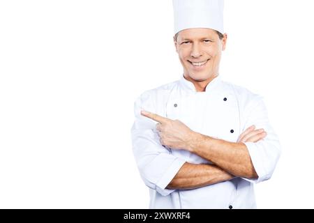 Sonderangebot vom Koch. Selbstbewusster, reifer Koch in weißer Uniform, der vor weißem Hintergrund nach vorne zeigt und lächelt Stockfoto