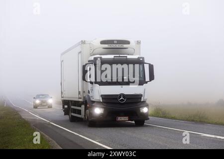 Der weiße Mercedes-Benz Antos Truck Thermo King Anhänger taucht beim Transport von Gütern auf der Autobahn 9 aus dem Nebel auf. Humppila, Finnland. August 2024. Stockfoto