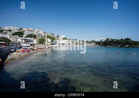 Ulcinj, Montenegro - 13. Juli 2024: Eine belebte Strandszene, die Menschen an einem Sandstrand mit klarem Wasser, leuchtenden Sonnenschirmen und einem Küstenabschnitt fängt Stockfoto