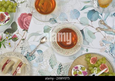 Vintage Teeparty im britischen Stil: Zwei Tassen Tee, Obst, dreieckige Teesandwiches, ein Scone mit Marmelade und Cupcakes auf Plateau. Draufsicht. Stockfoto