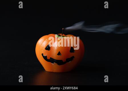 Eine Kerze mit Jack-o-Laterne im Halloween-Stil, die kürzlich ausgeblasen wurde, mit einer Rauchspur vor dunklem Hintergrund. Stockfoto