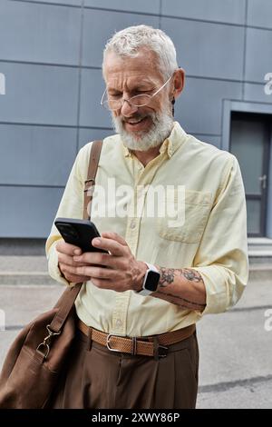 Ein bärtiger Mann lächelt, während er sein Smartphone überprüft, während er aus einem modernen Gebäude geht. Stockfoto