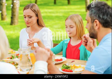 Ich danke Gott für das Essen. Familie hält Hände und betet vor dem Abendessen, während sie draußen am Tisch sitzt Stockfoto