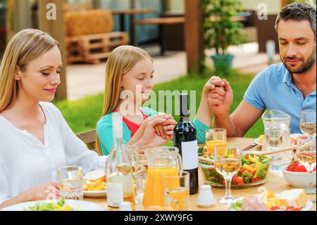 Danke für das Essen. Familie hält Hände und betet vor dem Abendessen, während sie draußen am Tisch sitzt Stockfoto