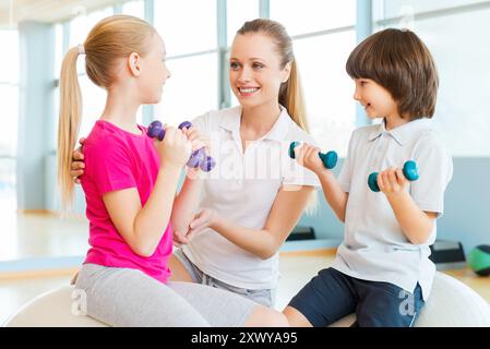 Lehrer mit Kindern. Fröhlicher Instruktor hilft Kindern beim Training im Health Club Stockfoto