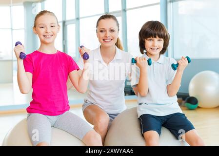 Lehrer mit Kindern. Fröhlicher Instruktor hilft Kindern beim Training im Health Club Stockfoto