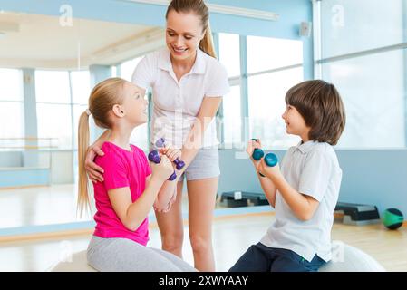 Kinder beim Training unterstützen. Fröhlicher Instruktor hilft Kindern beim Training im Health Club Stockfoto