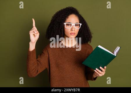 Porträt der hübschen jungen Frau Buch Punkt Finger tragen Pullover isoliert auf Khaki Farbe Hintergrund Stockfoto