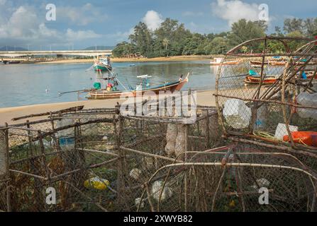 Fischfallen stapelten sich am Ufer mit einem Fischerboot im Hintergrund. Leere Fallen, die sich am Meer auftürmen und zum Angeln bereit sind. Stockfoto