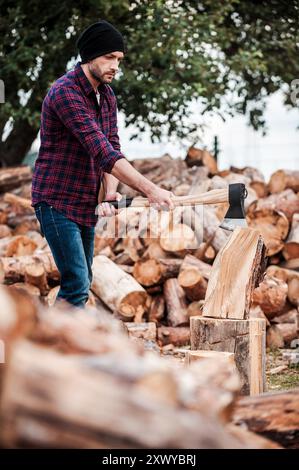 Selbstbewusster Holzarbeiter. Ernstzunehmender junger Forstwirt, der im Freien Baumstämme schneidet Stockfoto