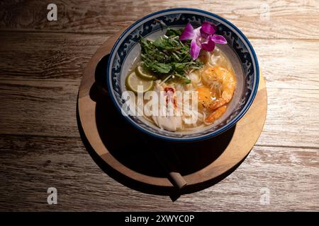 Hühnergarnelen-Pho-Nudelsuppe in einer Schüssel mit Limette und violetter hawaiianischer Orchideenblüte Stockfoto