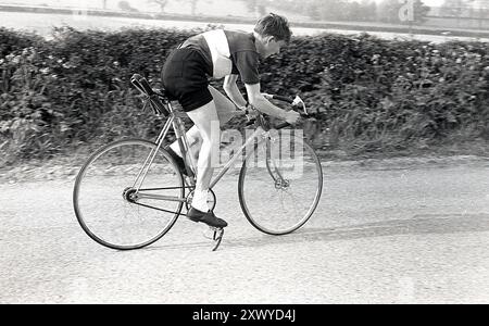 1960er Jahre, historischer junger Mann männlicher Radfahrer auf der Straße, Ersatz für Reifen im Sattel, England, Großbritannien. Radfahren mit dem „Southern“-Fahrrad, Fahrrad mit fester Ausrüstung, den rechten Fuß aus Clips, Radshorts aus Wolle und Trikot Stockfoto