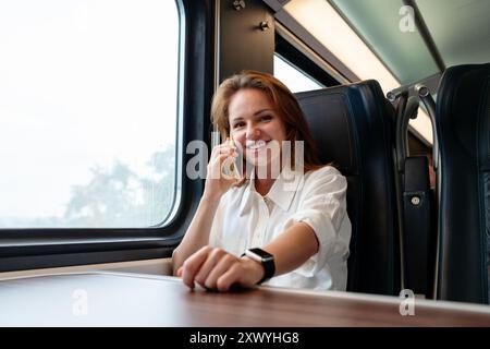 Junge Geschäftsfrau, die auf ihrem Handy spricht und während einer Geschäftsreise mit dem Zug lächelt. Stockfoto